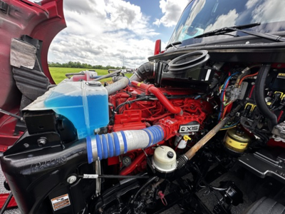 Kenworth T680 engine bay with red engine, blue coolant reservoir, blue hose, and various hoses and components visible