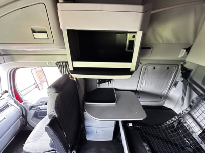 Interior cabin view of a 2022 Kenworth T680 showing a loft bunk area and table between seats, overhead storage, and side panels.