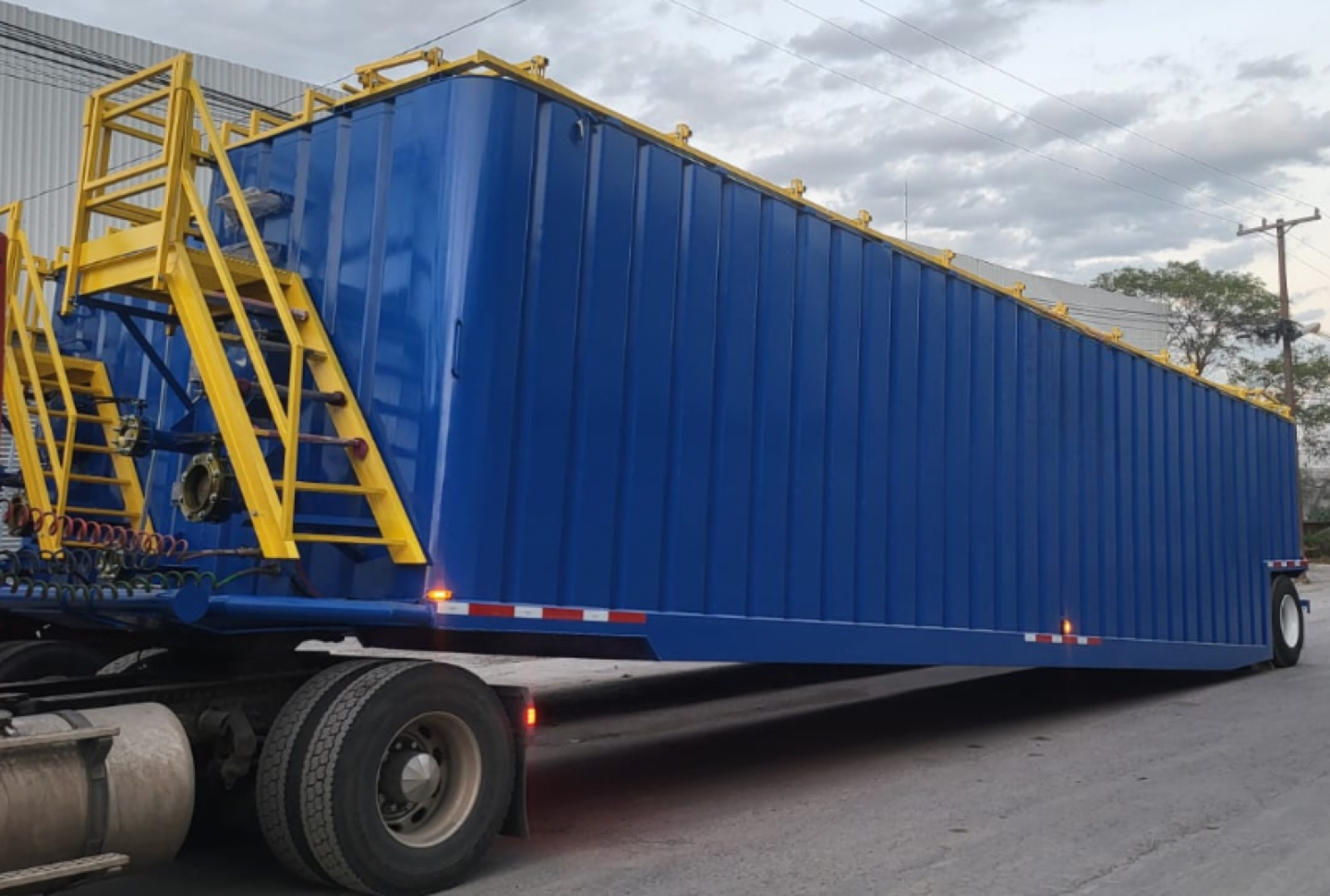 Fracturing trailer tanker in blue with yellow stairway and rails, mounted on a heavy truck trailer.