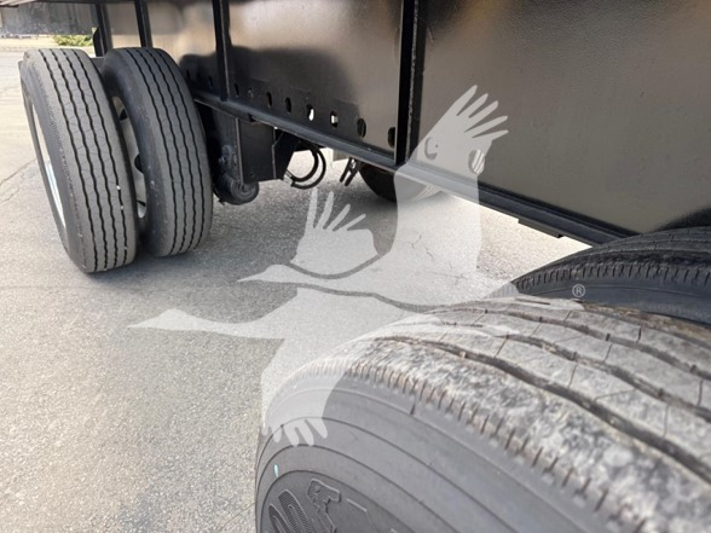 Trailer rear axle with dual left tires and slide mechanism visible under a flatbed.