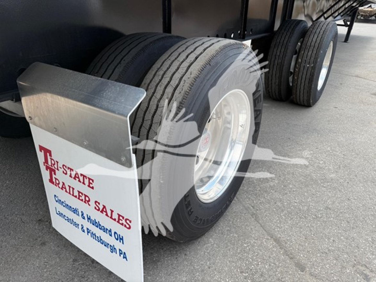 Trailer rear axle area showing dual tires and a mud flap with Tri-State Trailer Sales logo and text