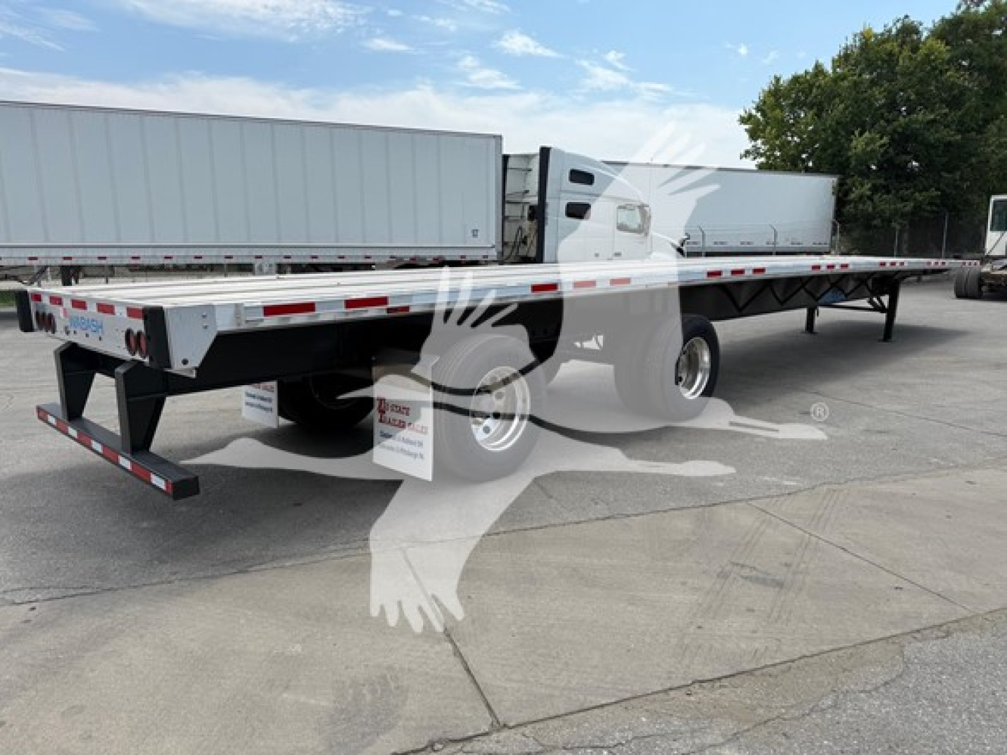 Flatbed trailer showing rear axle slide with Wabash branding, low-angle view, aluminum side rails, tandem axles, reflective tape, and landing gear.