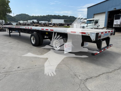 Flatbed trailer with rear axle slide showing aluminum deck, dual rear axles, and reflective safety stripes. VIN decal and stock number SC447895 visible near front.