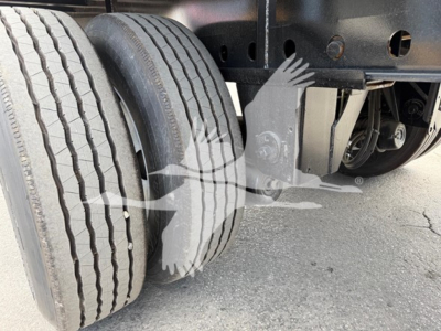 Trailer rear axle area showing dual wheels and frame components under a flatbed trailer with suspension and leaf springs visible.