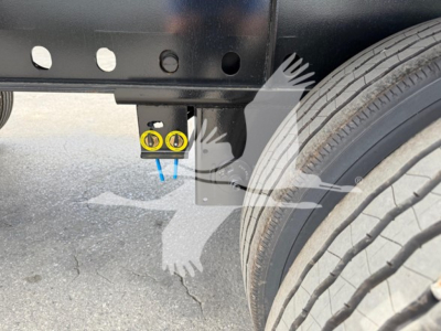 Trailer undercarriage showing wheel, frame, and a yellow tow eye/connector with blue straps or pins.