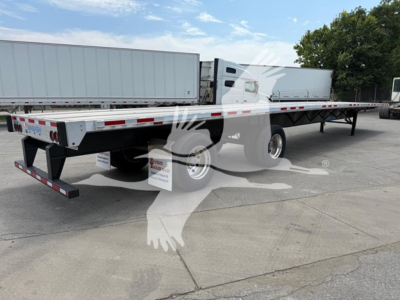 Flatbed trailer showing rear axle slide with Wabash branding, low-angle view, aluminum side rails, tandem axles, reflective tape, and landing gear.