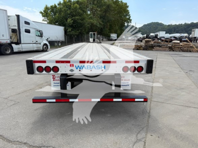 Trailer rear view showing Wabash flatbed trailer with rear axle slide and taillights, license plate area, and reflective bumper.