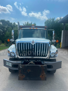 Front view of a blue/white 2008 International 7400 dump truck showing large chrome grille, bumper, headlights, and a rusty dump blade; windshield with side mirrors and clearance lights.