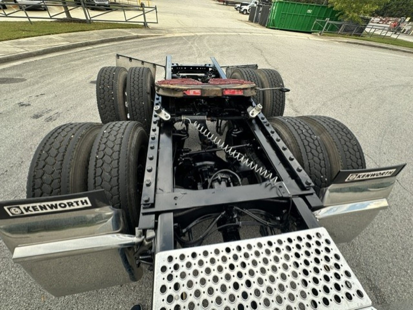 Kenworth truck chassis view showing fifth wheel, dual rear axles, and pogo-style suspension with two sets of dual tires, image focuses on rear frame and steps.