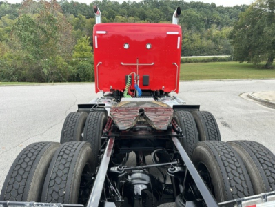 Kenworth T880 chassis rear view showing dual rear axles and air lines with fifth wheel absent. Red cab section with back of sleeper and exhaust stacks visible.