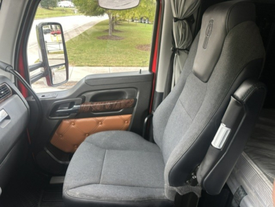 Kenworth truck interior front seat and door panel showing gray fabric seat, armrest, and wood-grain trim; side mirror visible through window.