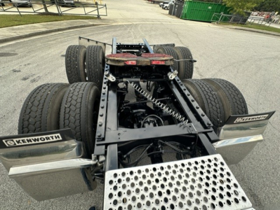 Kenworth truck chassis view showing fifth wheel, dual rear axles, and pogo-style suspension with two sets of dual tires, image focuses on rear frame and steps.