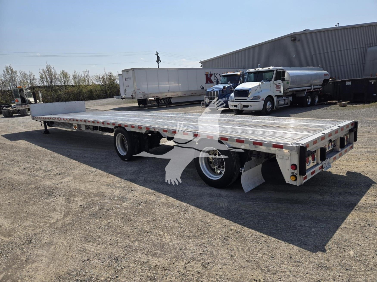 2019 Reitnouer Dropmiser trailer in an outdoor lot, flatbed with dual rear axles, brake lights, silver aluminum decking, and a white cab truck in background.