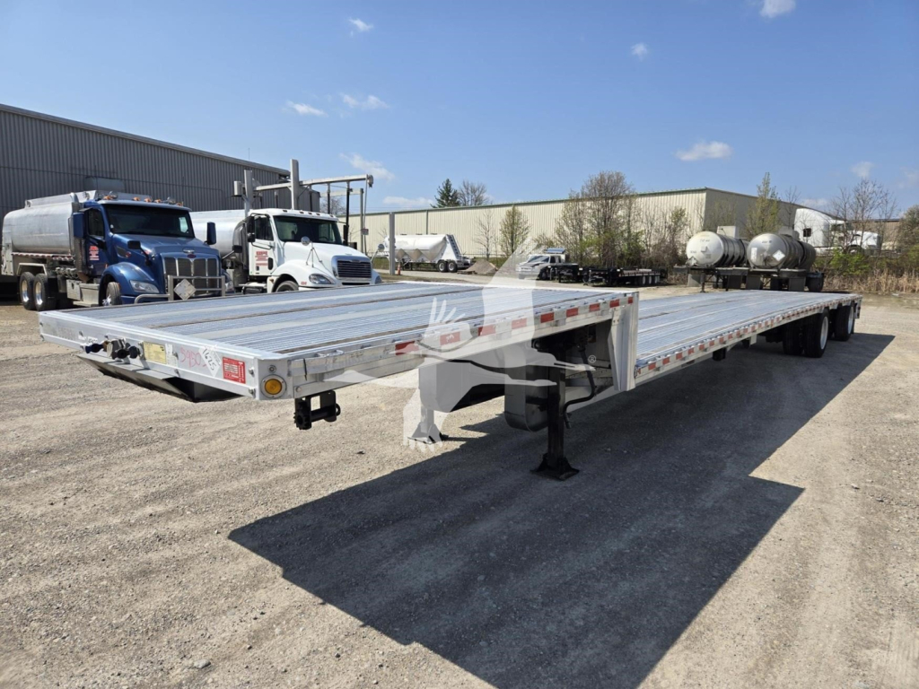 Trailer deck showing dropdeck trailer with metal platform, dual sets of wheels, and support legs. Branding and reflective tape along sides.