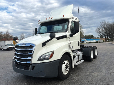 Front-left side view of a white Freightliner Cascadia126 day cab truck with raised sleeper, showing chrome grille, tall aerodynamic mirrors, and dual rear axles.