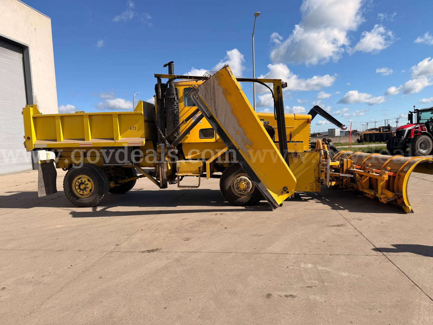 Oshkosh PA-2523-3 plow truck with front-mounted conveyor and yellow equipment, side view showing hydraulic lift and plow attachment.