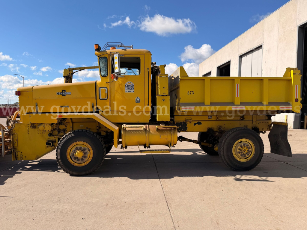 Mobile dump truck in yellow with plow attachment, Oshkosh PA-2523-3, side view showing cab, large dump bed, and 