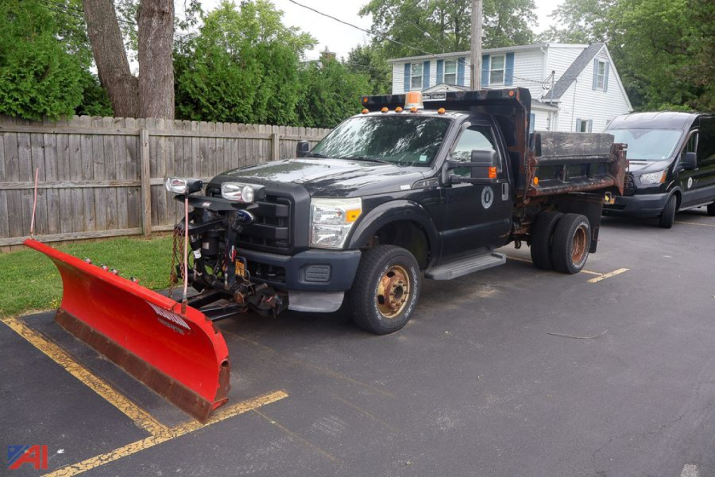 Tow-focused image of a black 2011 Ford F-350 Super Duty dump truck with a red snow plow attachment in front, orange warning lights on cab roof, and a flatbed/dump bed behind.
