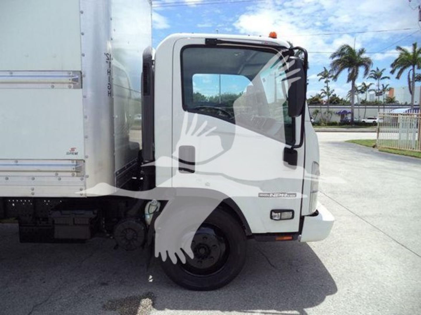 Isuzu NPR-HD box truck cab and front wheel visible; no legible model text on door; partial side of cargo box; silver/gray truck with black tires; clear sky.