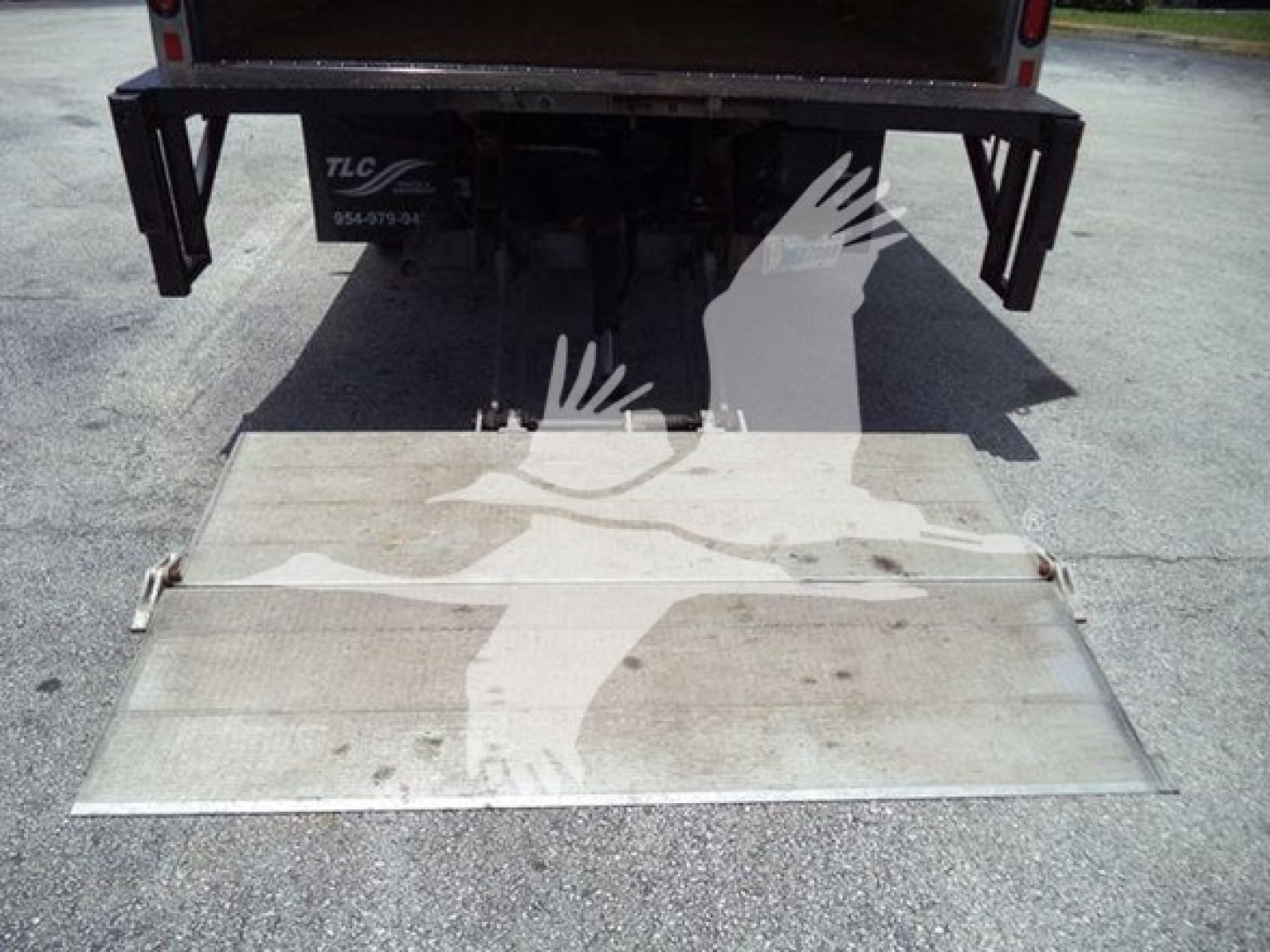 Isuzu NPR HD box truck rear view showing lowered Euro-style aluminum loading ramp/step with shadowed vehicle tail and hitch area.