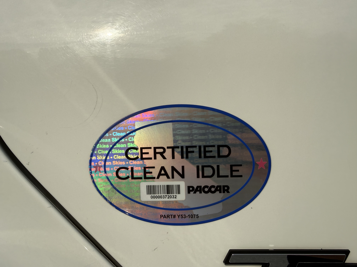 Certification sticker on a white surface with holographic oval text: 'CERTIFIED CLEAN IDLE' and small barcode. Partial text 'PACCAR' beneath.