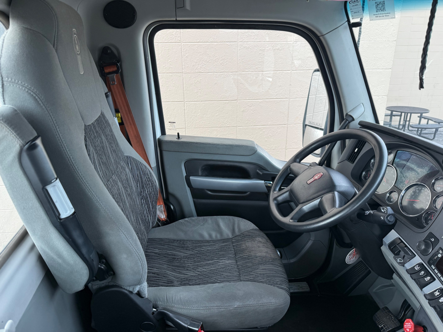 Cab interior of a 2022 Kenworth T680, front driver seat and steering wheel visible, dashboard with gauges, gray fabric seats.