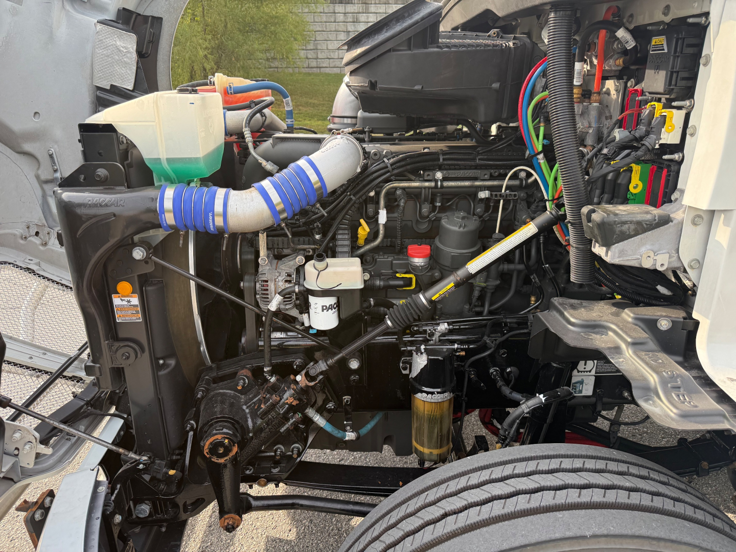 Kenworth T680 engine bay with visible coolant reservoir, hoses, wiring harnesses, and engine components.