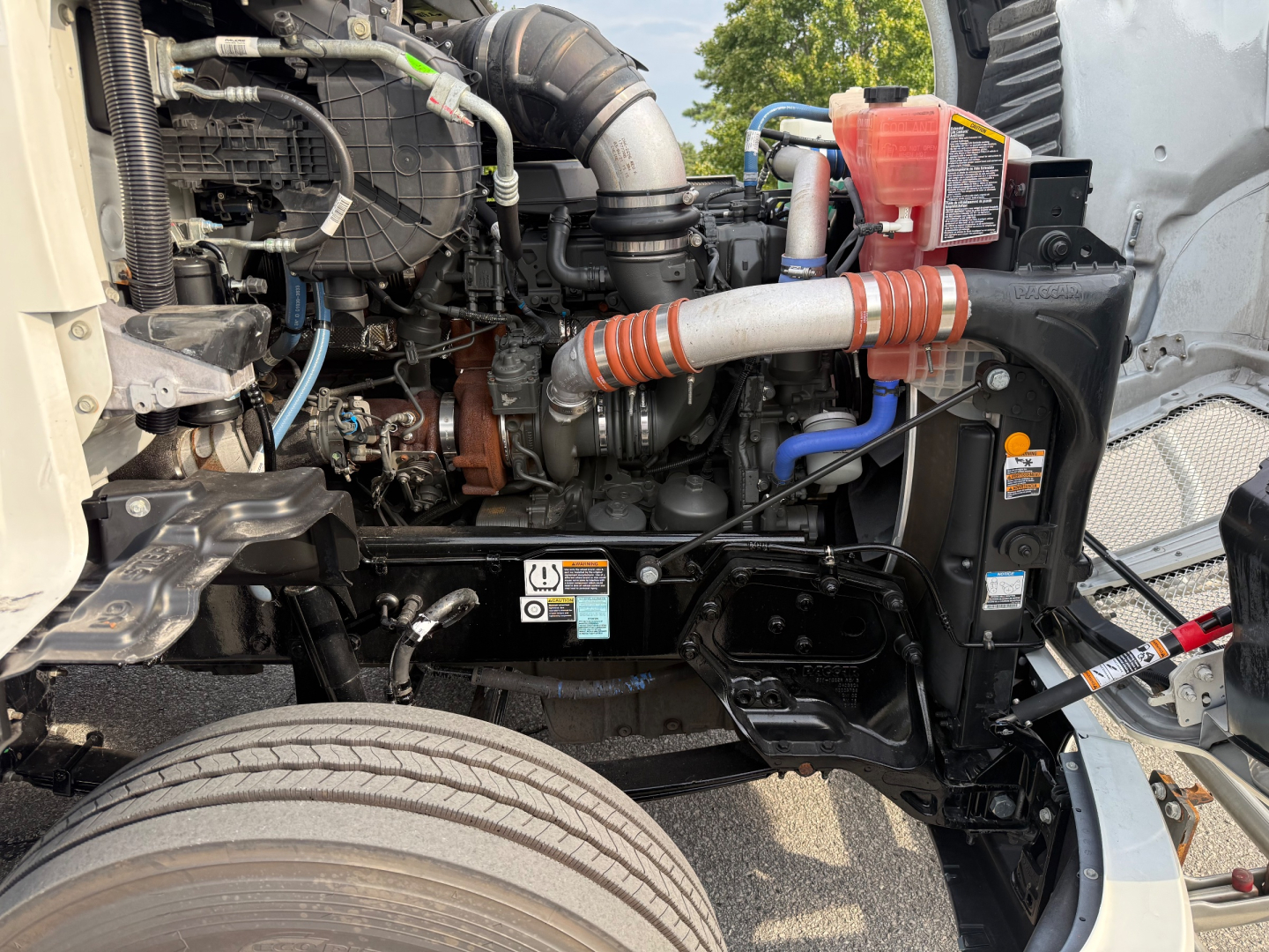Kenworth T680 engine bay showing coolant reservoir, hoses, and various engine components.