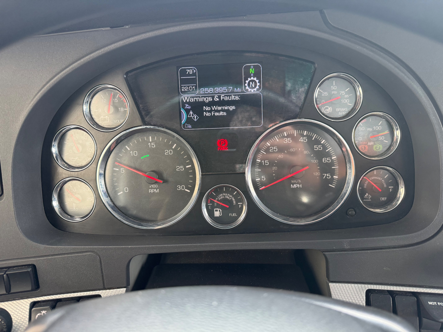 Kenworth T680 instrument cluster view showing gauges and digital display with warnings, steering wheel bottom center
