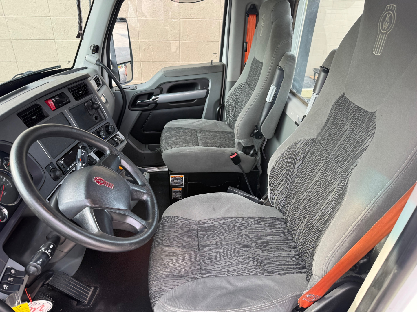 Kenworth T680 cab interior showing steering wheel, driver seat, and dashboard with control panels.