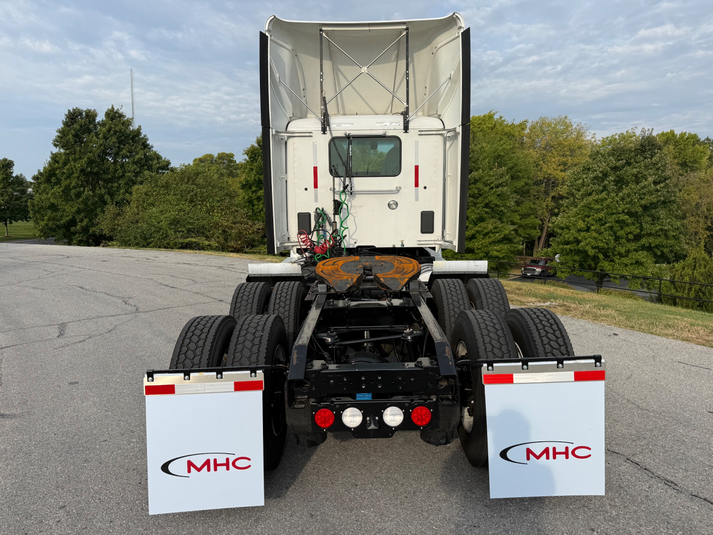 Kenworth T680 rear view showing chassis, dual rear axles, mud flaps with MHC logos, and spare tire storage area.