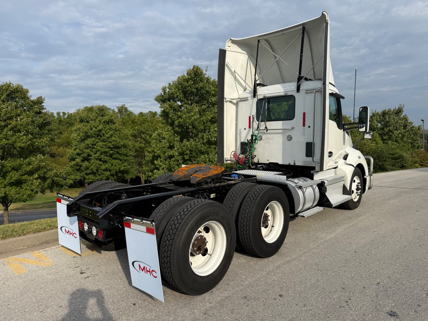 Kenworth T680 tractor truck seen from rear-three-quarter view with exposed fifth-wheel area and dual rear axles. Visible labels: MHC logos on mud flaps at rear.