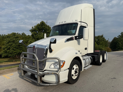 Kenworth T680 conventional daycab tractor in white, front chrome grille with grille guard, large sleeper cab top, dual rear axles, side mirrors, fuel tanks, and tires visible.