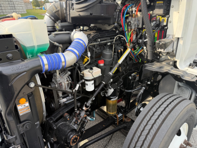 Kenworth T680 engine bay showing blue intake hose, wiring harnesses, fluid reservoirs, and diesel engine components.