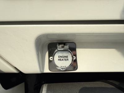 Kenworth T680 engine bay area showing engine heater cap labeled ‘ENGINE HEATER’ mounted in a recessed panel on the front lower bumper.