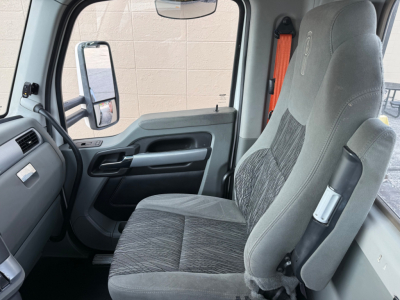Kenworth truck interior cab front seat and door panel. Grey fabric driver's seat with memory/adjuster, black door handle, window controls, large side mirror visible through window.
