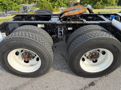 Dual rear axles of a Kenworth T680 chassis showing two large wheels and tires with white rims, fifth wheel and drivetrain components visible between.