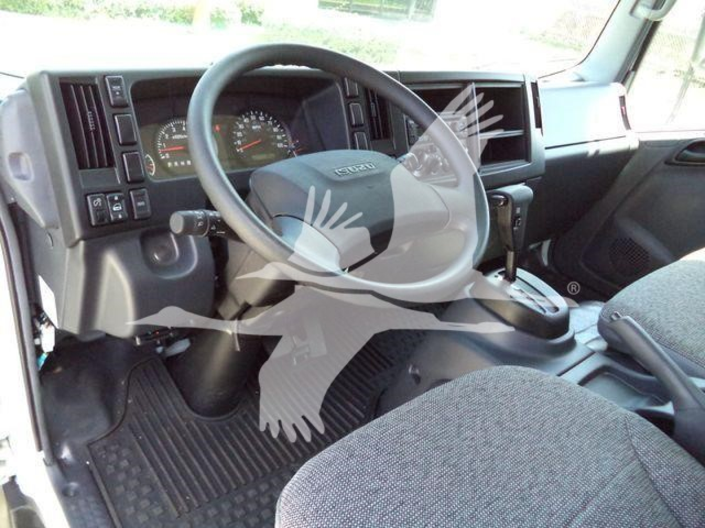 Isuzu NPRR cab interior showing steering wheel, dashboard with gauges, gear selector, and driver seat in a rolloff truck.