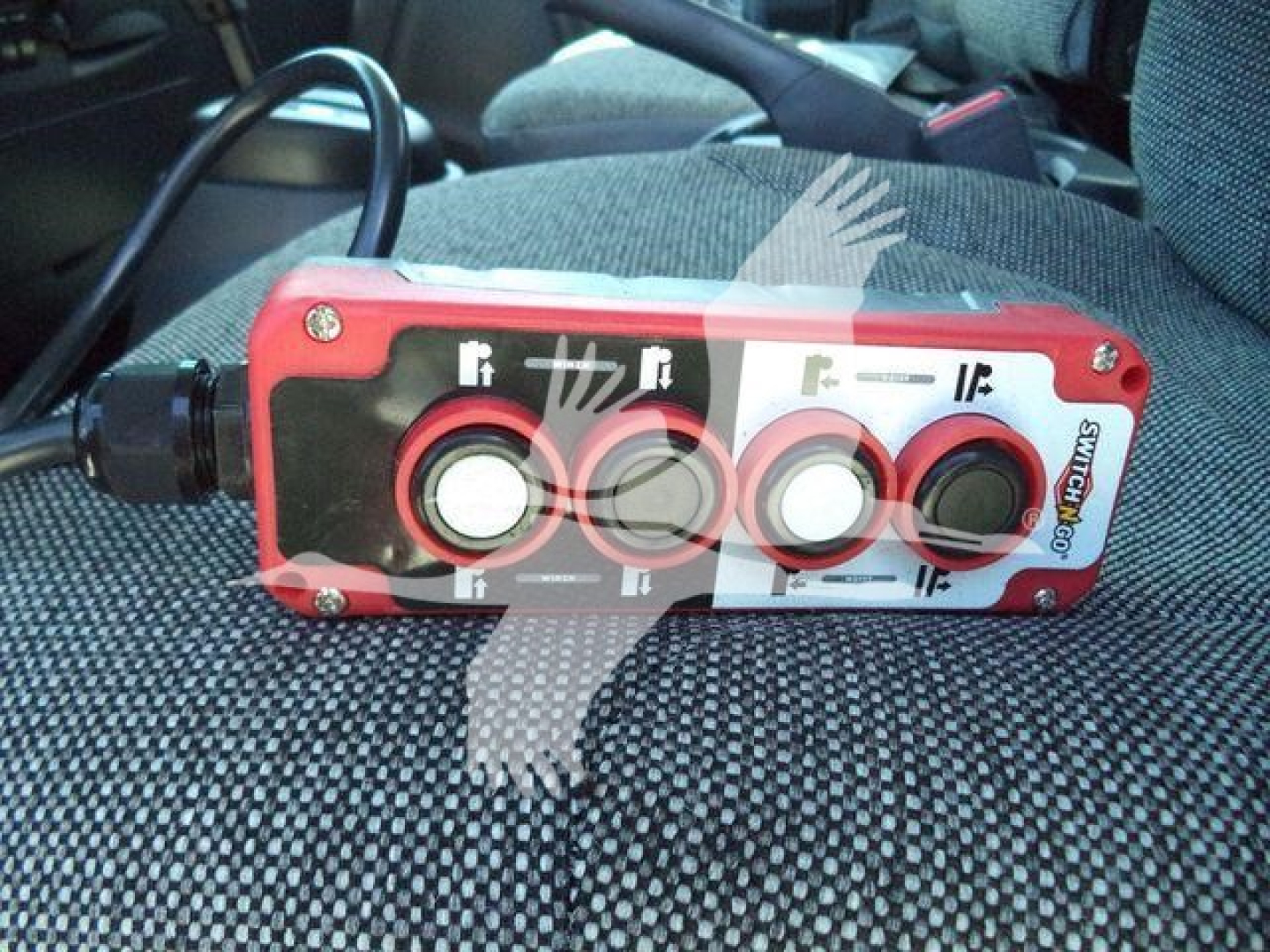 Trucker control pendant showing four circular knobs and indicator icons, red housing with black and white panel.