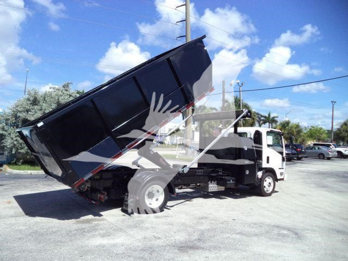 Isuzu NPR/NRR-style dump truck with a raised bed in a lot; no legible labels visible on the truck from this angle.