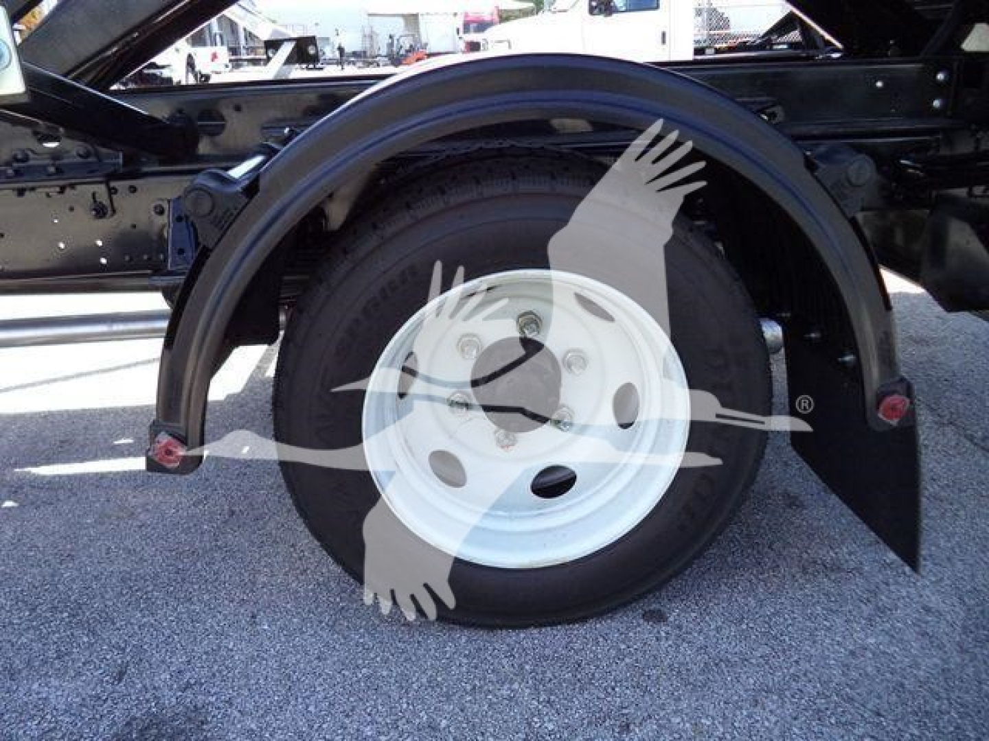 Isuzu NRR rolloff truck rear wheel assembly showing white steel wheel, tire, and fender with surrounding chassis components.