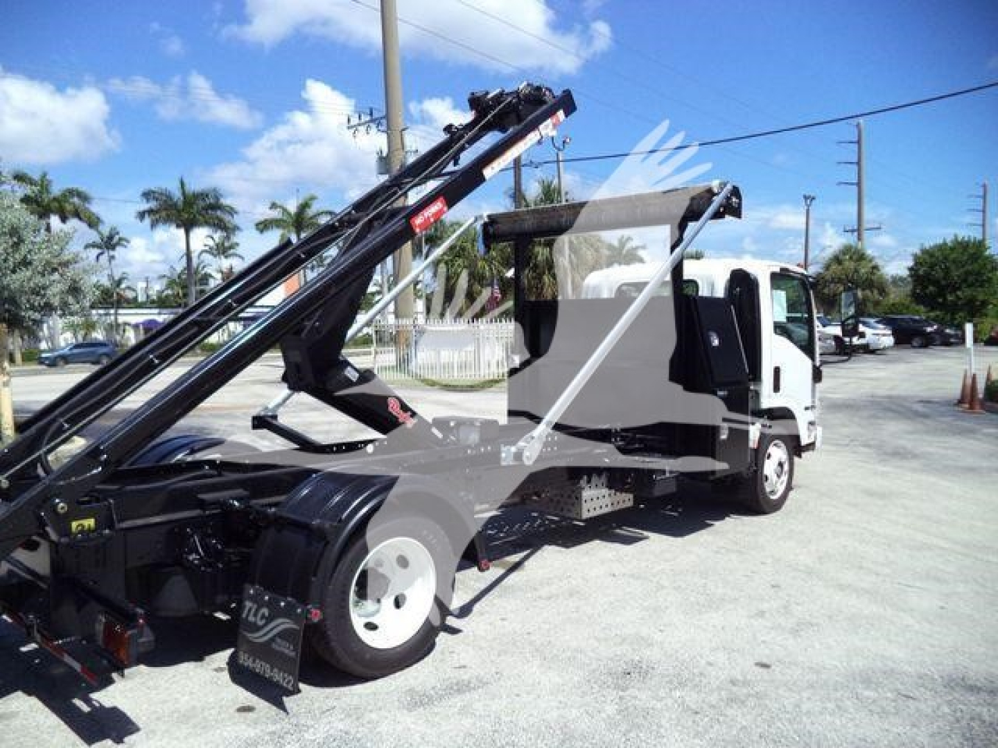 Isuzu NRR roll-off truck side view showing hydraulic boom arms and flatbed with white cab.