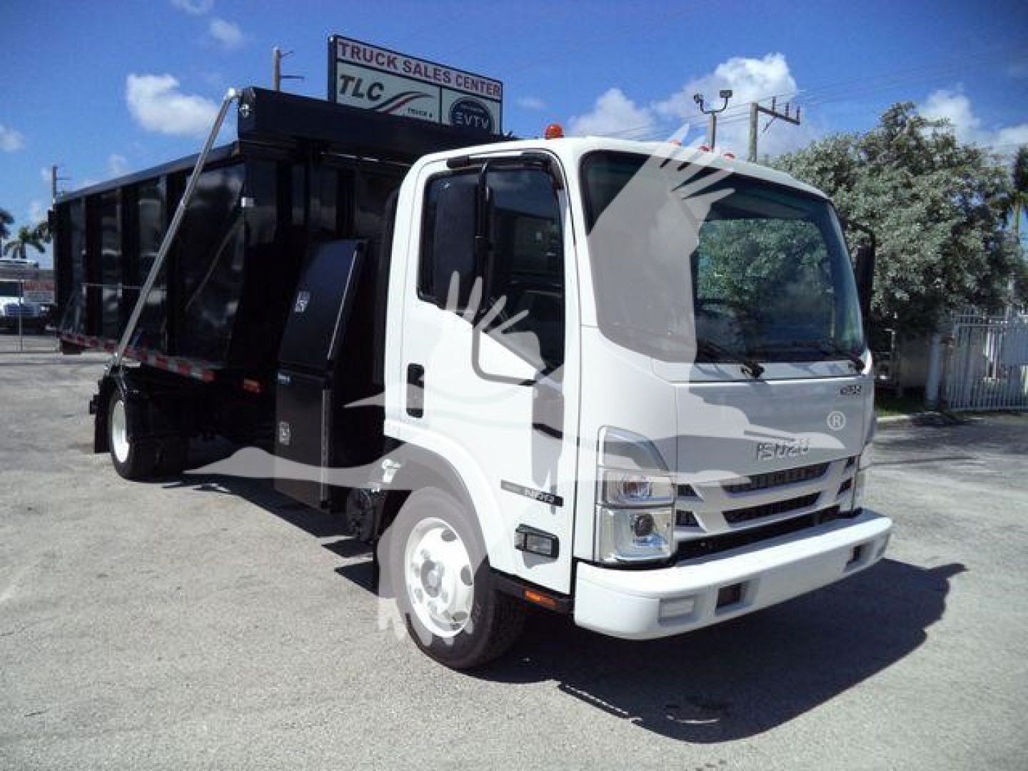 Isuzu NPRR rolloff truck in white cab with black bed, front grille and headlights visible, side view showing cargo bed and rear wheels.