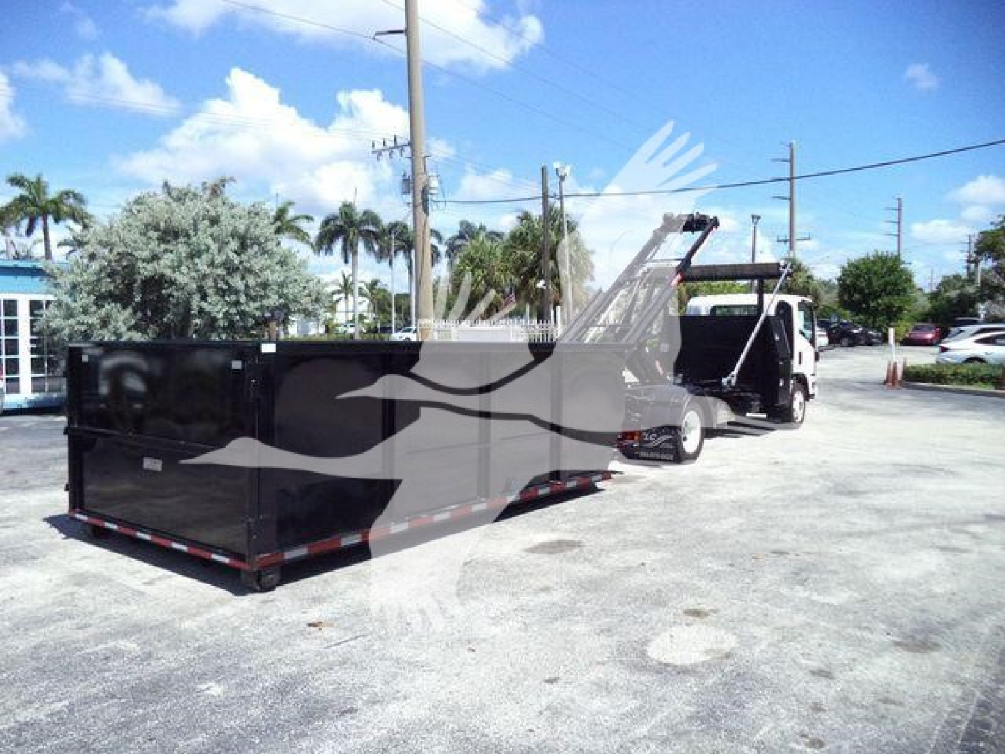 Isuzu NPRR roll-off truck with large black dump container attached to a white cab in a lot.