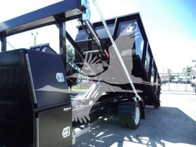 Isuzu NRR roll-off truck body with tilted cargo bed and hydraulic hoist in a dealership lot.