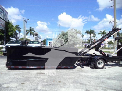 Isuzu NPRR roll-off truck body in service bay showing large black rectangular cargo bed with graphic silhouette and hydraulic arm.