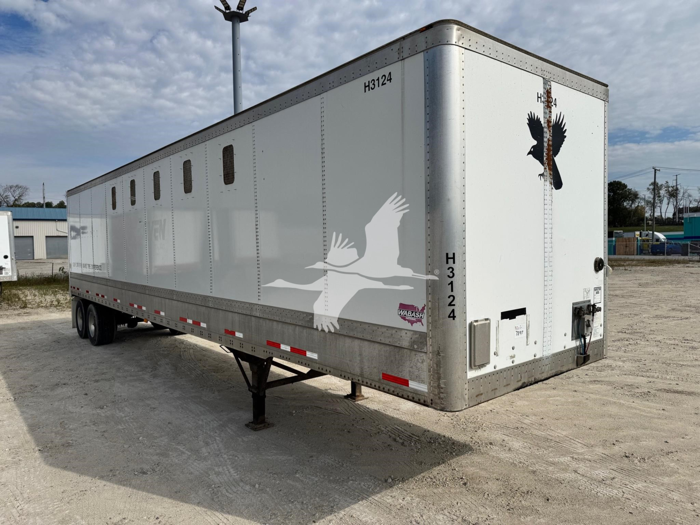 Trailer side and rear view showing a 2014 Wabash chip trailer with white body, bird graphics, and multiple vents along the side; rear door and support legs visible.