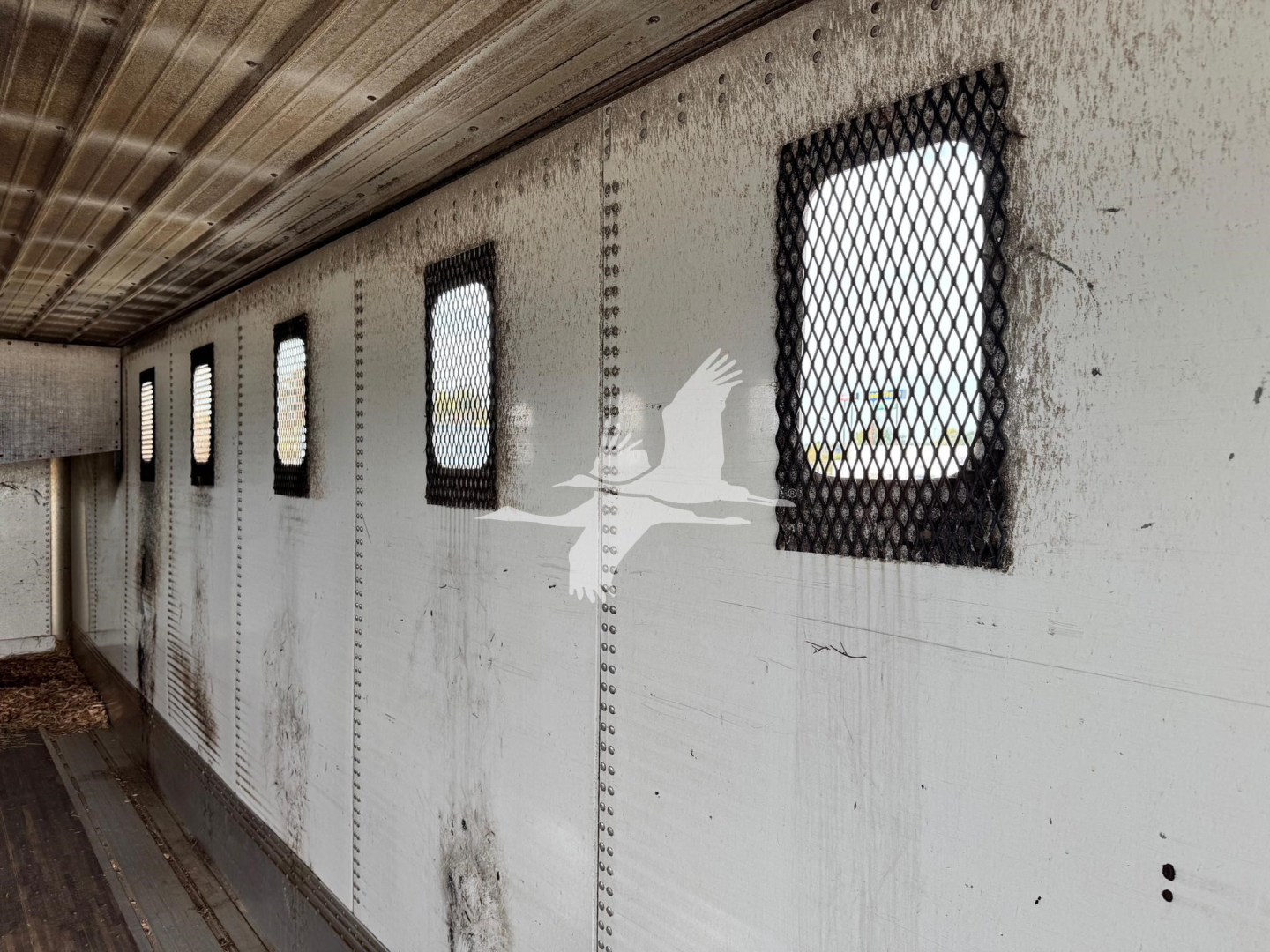 Trailer side interior with ventilation windows and metal mesh protecting openings; light gray walls, dirt smudges, riveted panels.