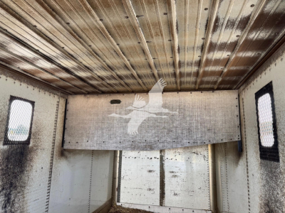 Trailer interior showing chipped trailer with metal walls and ceiling, small windows, rear hatch area, and chipped interior panels.