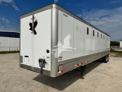 Trailer side and rear showing white Wabash chip trailer with small square windows, black chassis, and VIN tag; graphic of a flying eagle on rear door; stock number and other markings visible